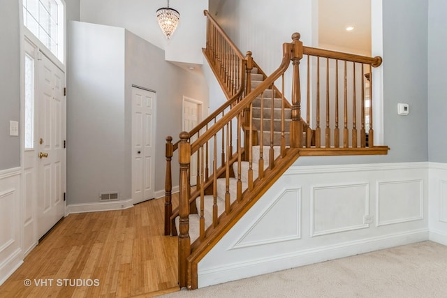 entryway with a decorative wall, a wainscoted wall, wood finished floors, visible vents, and an inviting chandelier