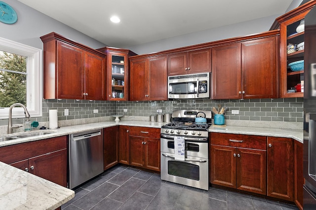 kitchen featuring a sink, appliances with stainless steel finishes, light stone countertops, tasteful backsplash, and glass insert cabinets