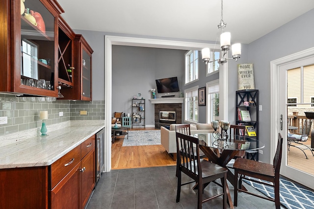 dining space featuring dark tile patterned floors, a chandelier, beverage cooler, and a glass covered fireplace