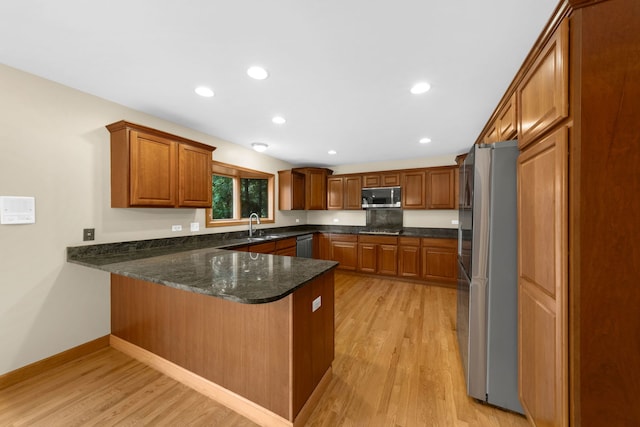 kitchen with appliances with stainless steel finishes, light wood-type flooring, dark stone counters, sink, and kitchen peninsula