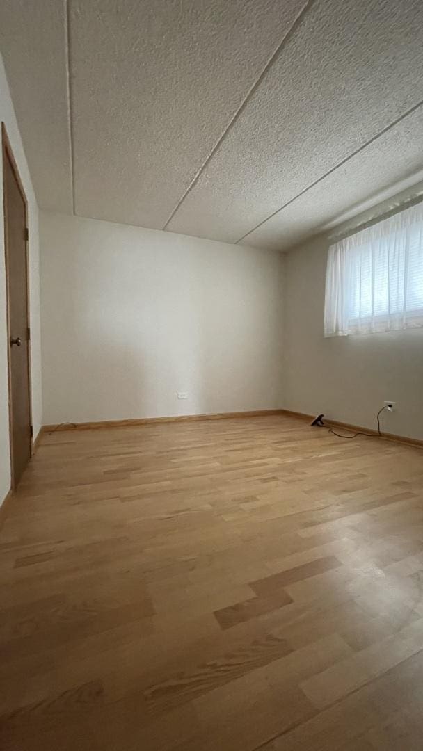 empty room featuring light wood finished floors, baseboards, and a textured ceiling