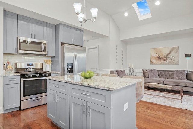 kitchen featuring lofted ceiling with skylight, hanging light fixtures, appliances with stainless steel finishes, dark hardwood / wood-style floors, and gray cabinets