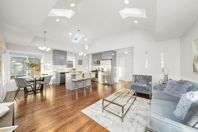 living room with sink, a skylight, high vaulted ceiling, dark hardwood / wood-style flooring, and a notable chandelier