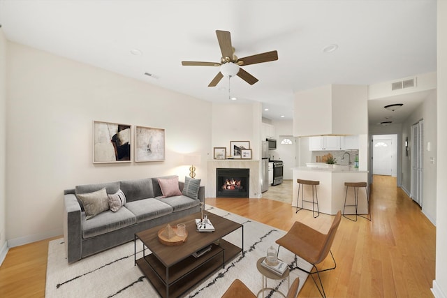 living area featuring a tile fireplace, baseboards, visible vents, and light wood finished floors