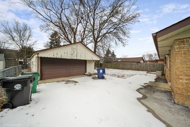 snow covered garage featuring a detached garage and fence