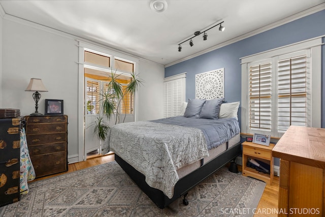 bedroom with rail lighting, crown molding, and wood finished floors