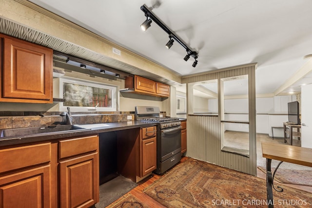 kitchen with stainless steel range with gas cooktop, refrigerator, dark countertops, dark wood-type flooring, and a sink