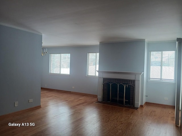 unfurnished living room featuring wood-type flooring, a brick fireplace, ornamental molding, and a healthy amount of sunlight