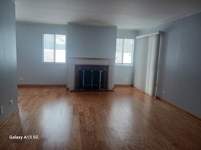 unfurnished living room with a brick fireplace, crown molding, baseboards, and wood finished floors