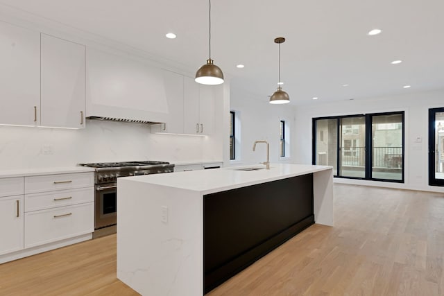 kitchen featuring a sink, white cabinets, high end stainless steel range oven, an island with sink, and decorative light fixtures