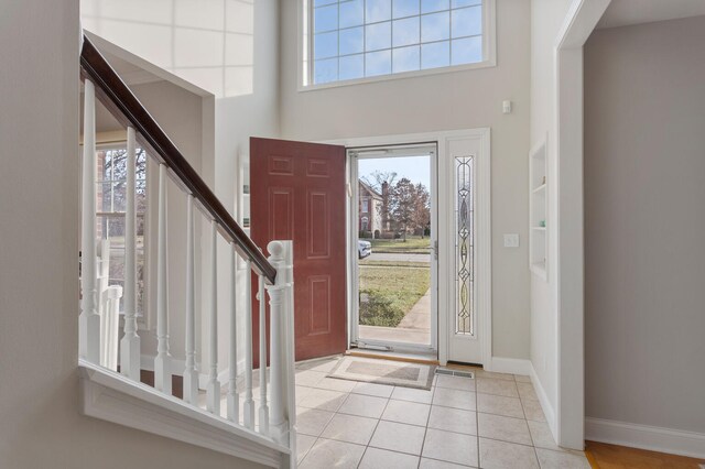 entrance foyer featuring baseboards, light tile patterned flooring, a towering ceiling, and a healthy amount of sunlight