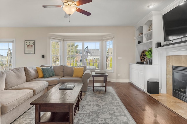 living room featuring built in shelves, plenty of natural light, a fireplace, and wood finished floors