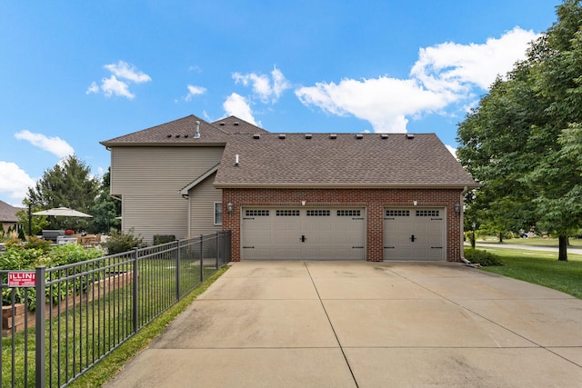 view of home's exterior with concrete driveway, brick siding, fence, and roof with shingles