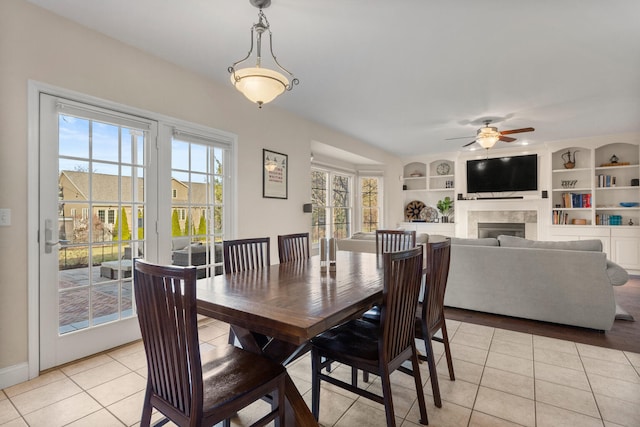 dining room with built in shelves, a ceiling fan, a tile fireplace, and light tile patterned flooring