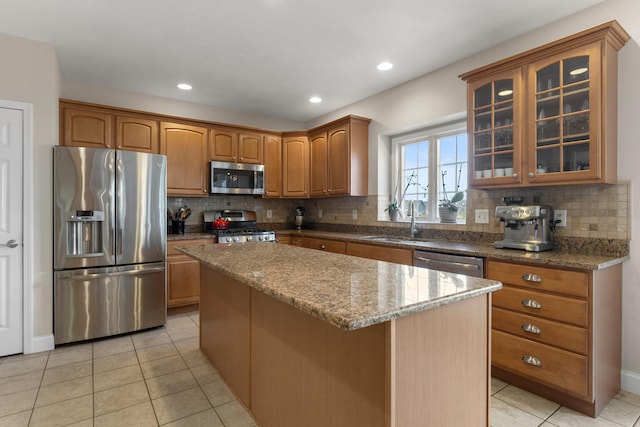 kitchen with a kitchen island, glass insert cabinets, appliances with stainless steel finishes, stone counters, and a sink