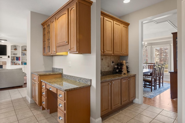 kitchen with light tile patterned floors, a fireplace, open floor plan, light stone countertops, and glass insert cabinets