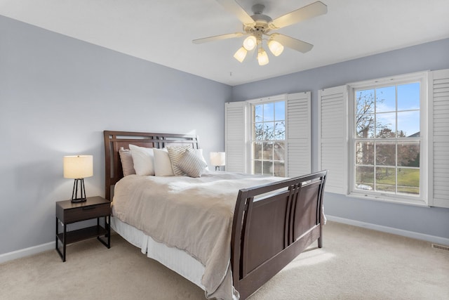 bedroom with light colored carpet, ceiling fan, baseboards, and multiple windows