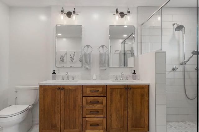 full bathroom featuring toilet, double vanity, a tile shower, and a sink