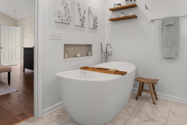 bathroom with lofted ceiling, marble finish floor, a soaking tub, and baseboards