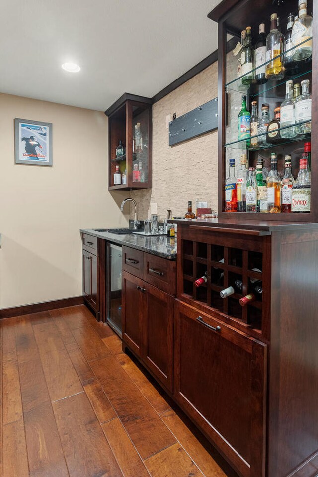 bar with dark wood finished floors, a sink, wet bar, beverage cooler, and baseboards