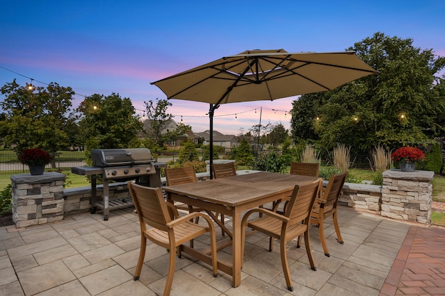 patio terrace at dusk with outdoor dining space, fence, and area for grilling