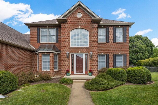 view of front of home with brick siding, roof with shingles, a front yard, and fence