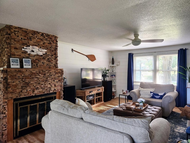 living room with hardwood / wood-style flooring, ceiling fan, a fireplace, and a textured ceiling