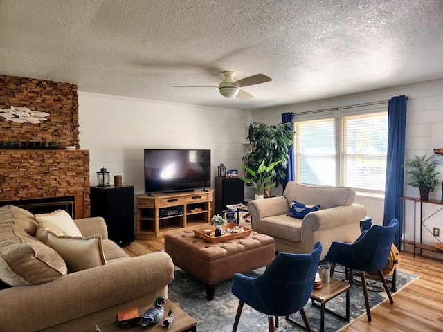 living room featuring a fireplace, light hardwood / wood-style flooring, a textured ceiling, and ceiling fan