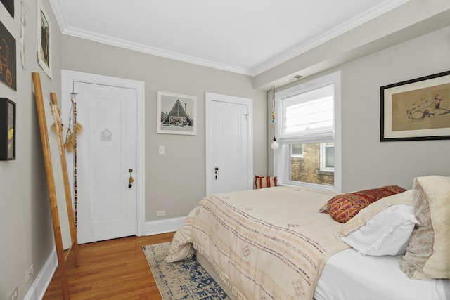 bedroom with visible vents, baseboards, crown molding, and wood finished floors