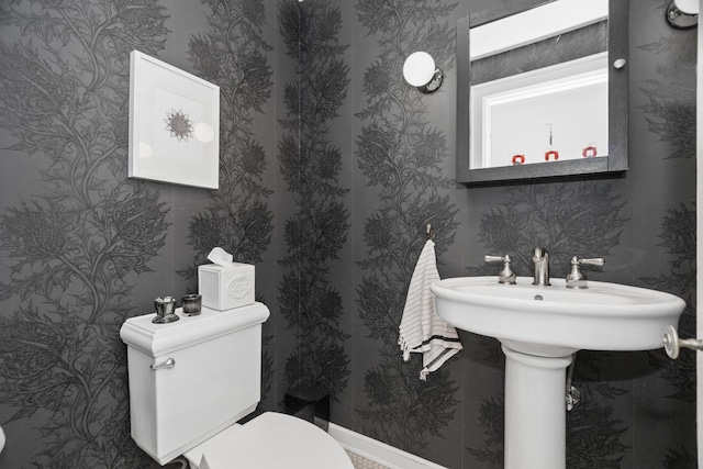 bathroom with toilet, wallpapered walls, and baseboards