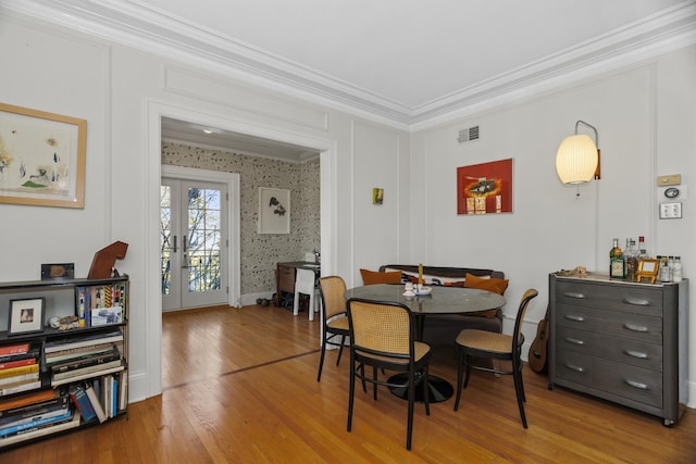 dining room with wood finished floors, visible vents, ornamental molding, french doors, and wallpapered walls