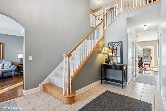 stairway with arched walkways, tile patterned flooring, and baseboards