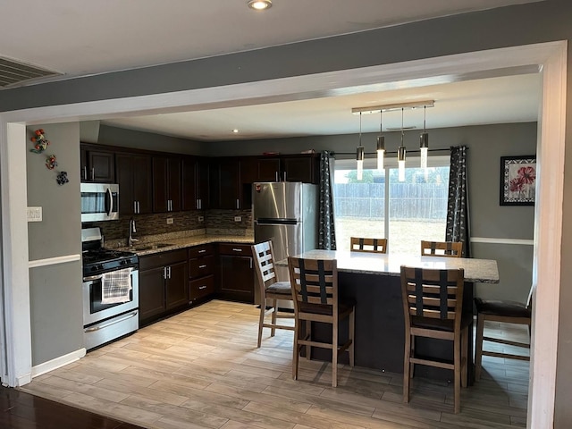 kitchen featuring stainless steel appliances, hanging light fixtures, a kitchen bar, and light stone countertops