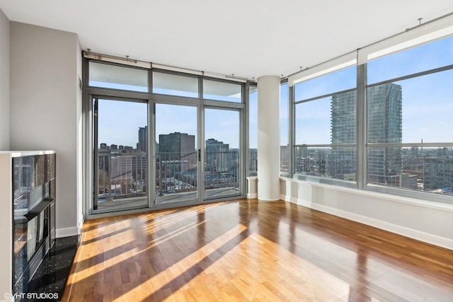 unfurnished room featuring a view of city, baseboards, a fireplace, and wood finished floors