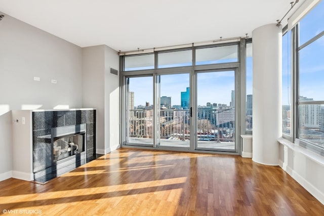 unfurnished living room featuring visible vents, a tile fireplace, wood finished floors, a view of city, and floor to ceiling windows