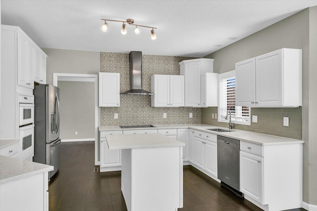 kitchen featuring white cabinets, wall chimney exhaust hood, appliances with stainless steel finishes, a center island, and a sink