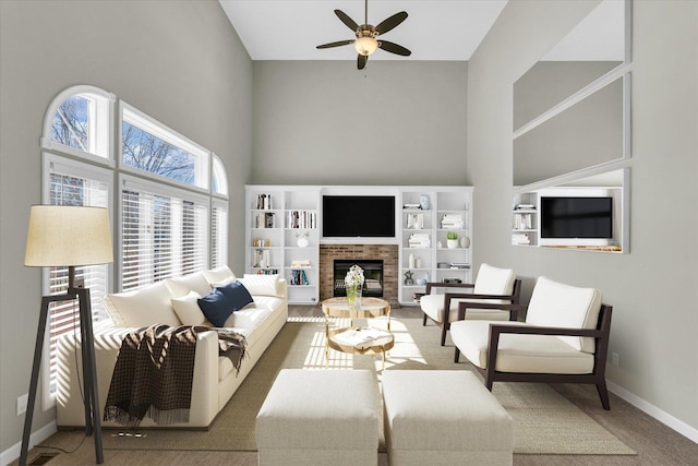 carpeted living area featuring a fireplace, a towering ceiling, baseboards, and ceiling fan