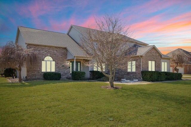 view of front of house with roof with shingles, brick siding, and a lawn