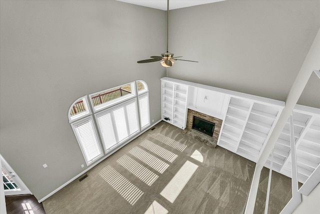 unfurnished living room with carpet floors, a fireplace, visible vents, a high ceiling, and ceiling fan