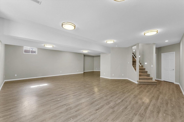 finished basement with a textured ceiling, wood finished floors, visible vents, baseboards, and stairs