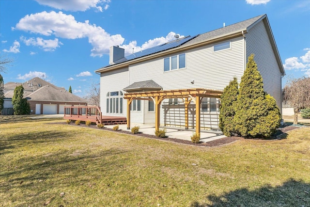 back of house featuring solar panels, a lawn, a deck, and a pergola