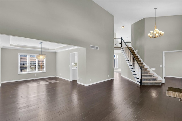 unfurnished living room with a chandelier, dark wood-type flooring, visible vents, baseboards, and stairs