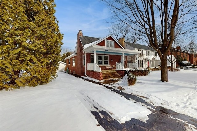 view of front facade with covered porch, a chimney, and brick siding