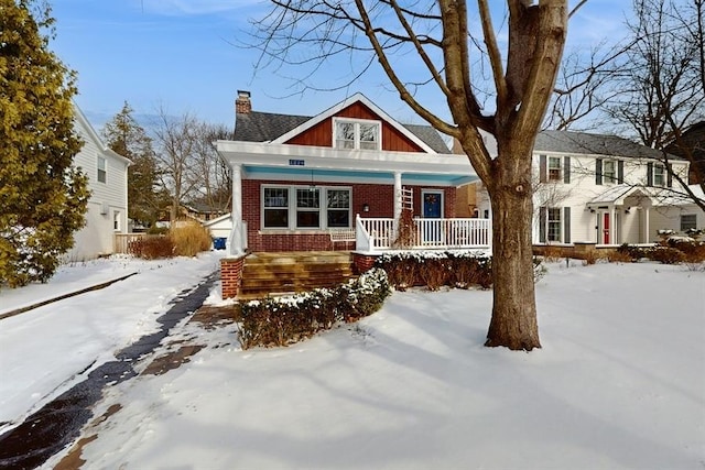 view of front of house featuring covered porch, brick siding, and a chimney