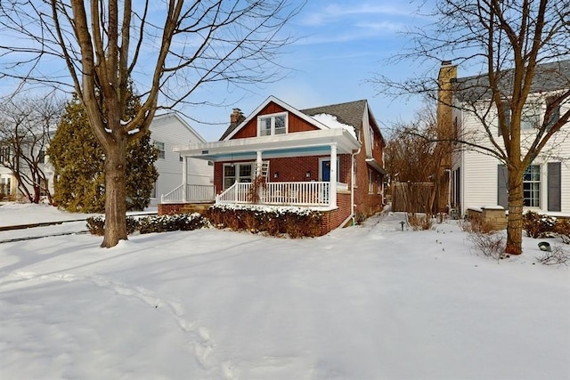 view of front facade with covered porch, a chimney, and brick siding