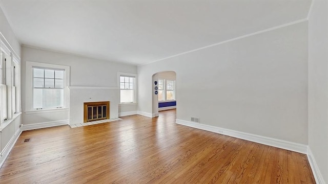 unfurnished living room featuring arched walkways, light wood-type flooring, a fireplace with flush hearth, and visible vents