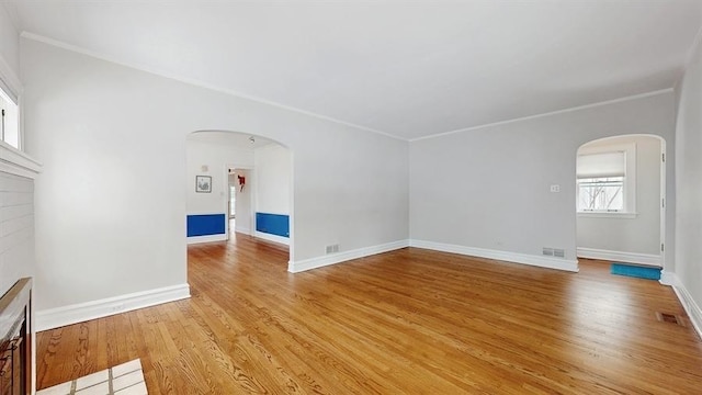 unfurnished living room with arched walkways, visible vents, light wood-style flooring, and baseboards