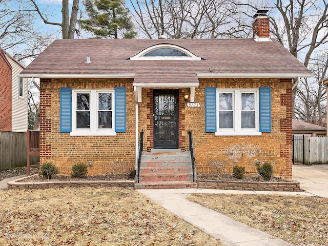 bungalow-style home featuring brick siding, a chimney, a shingled roof, and fence