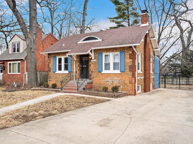 bungalow-style house featuring brick siding, fence, concrete driveway, roof with shingles, and a chimney