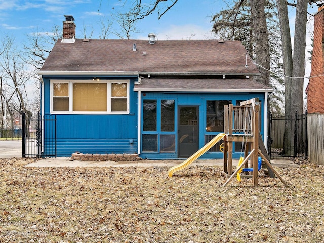 rear view of house with a playground, fence, a chimney, and roof with shingles